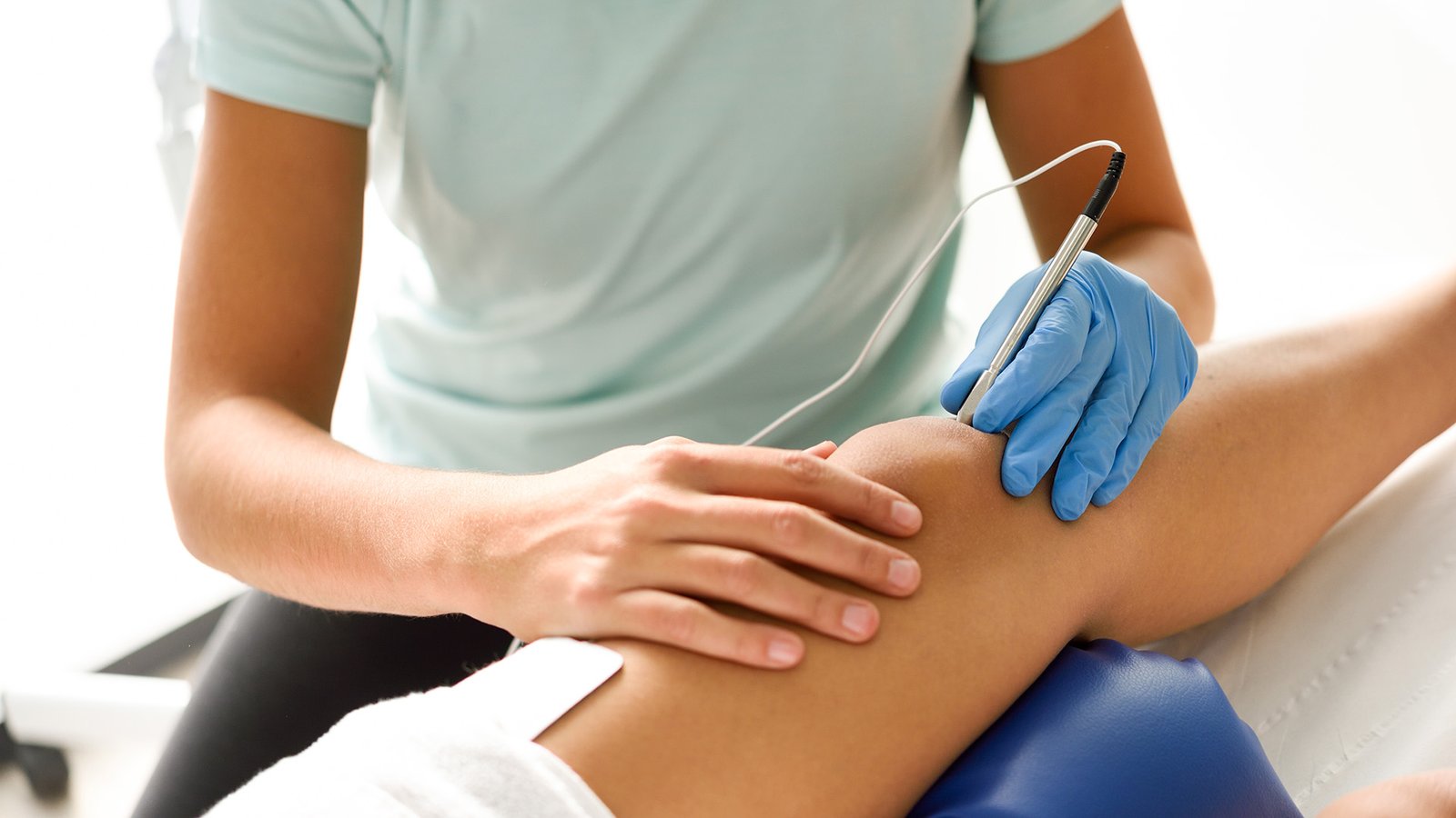 Electroacupuncture dry with needle connecting machine used by acupunturist on female patient for acupuncture guided by EPI Intratissue Percutaneous Electrolisis. Electro stimulation in physical therapy to knee of a young woman in physiotherapy center.